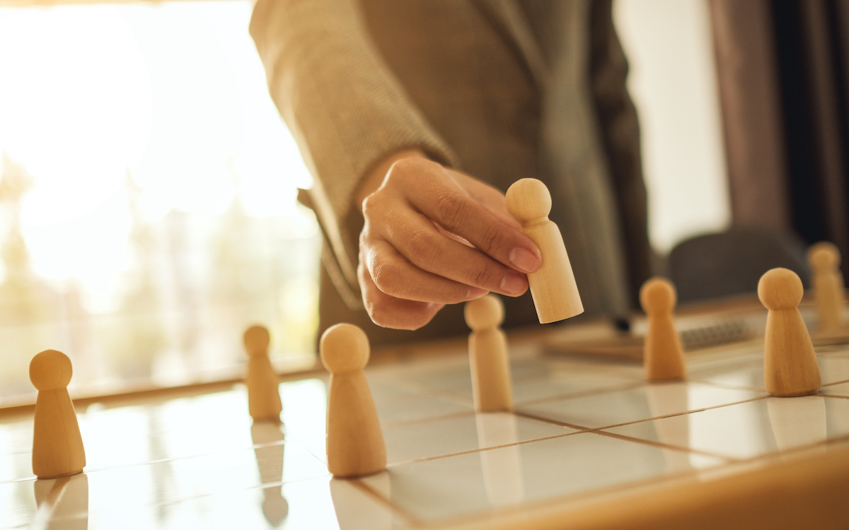 Business woman including wooden figures on team planning board 