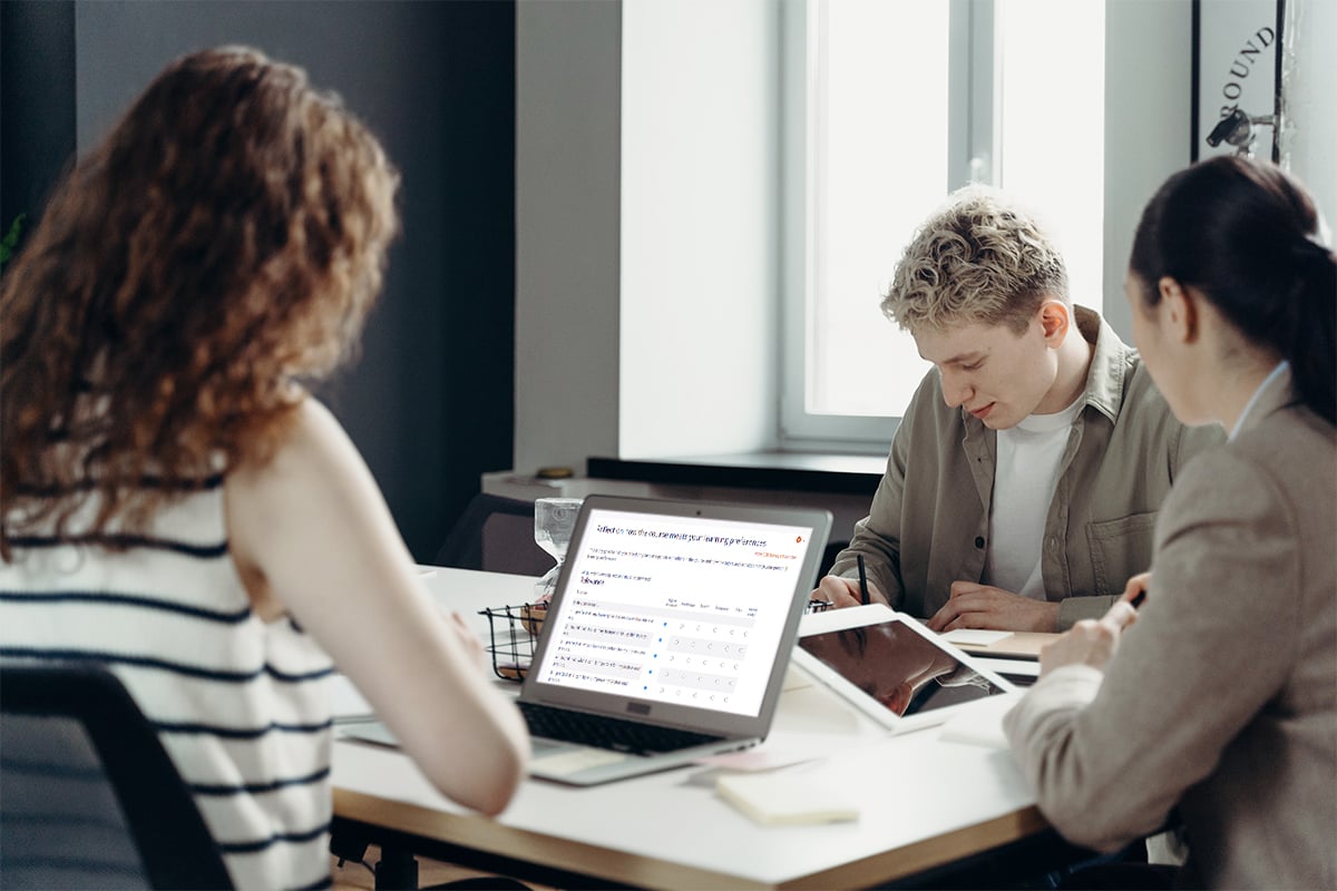 Three people sitting at a desk reading their work. 