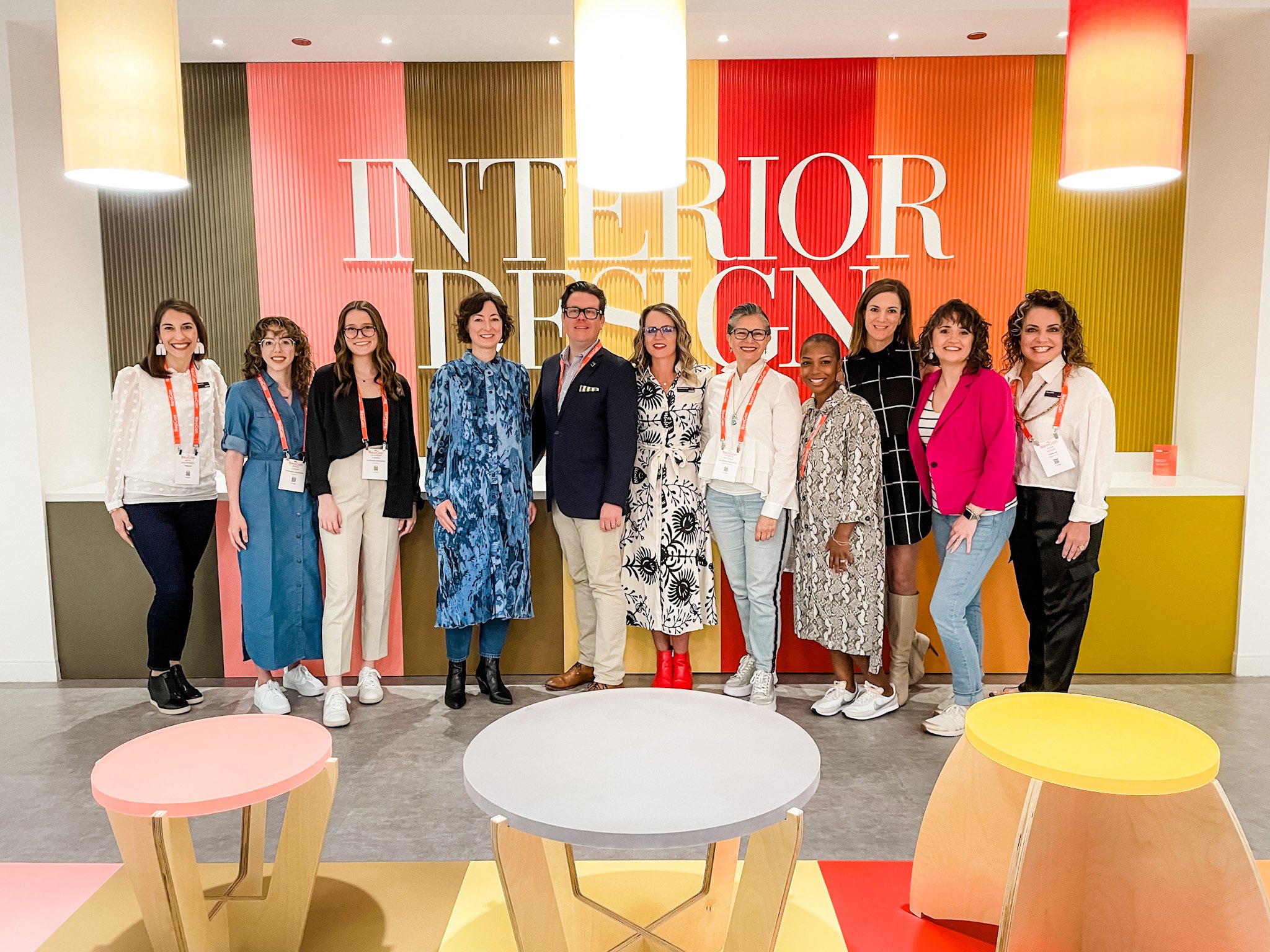 ThinkLab Trendspotters team gathers in front of a vibrantly colored wall emblazoned with Interior Design at NeoCon 2022